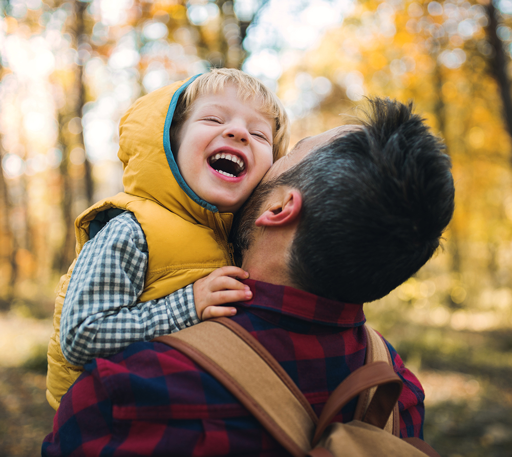 Very happy-looking boy being carried by his father in the woods